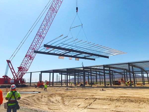 Steel roof structure being hoisted by crane at a large-scale commercial building construction site.